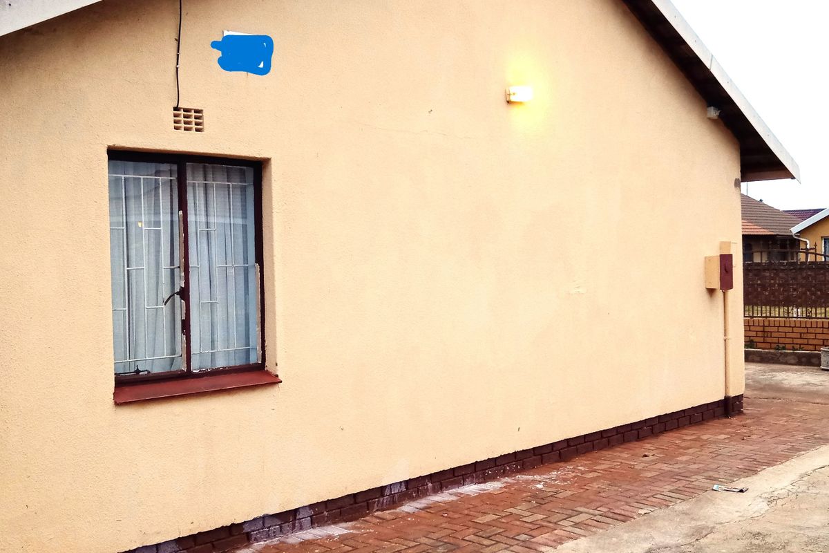 A view of the rear exterior wall featuring brick paving, a window with security bars, and an external wall light.