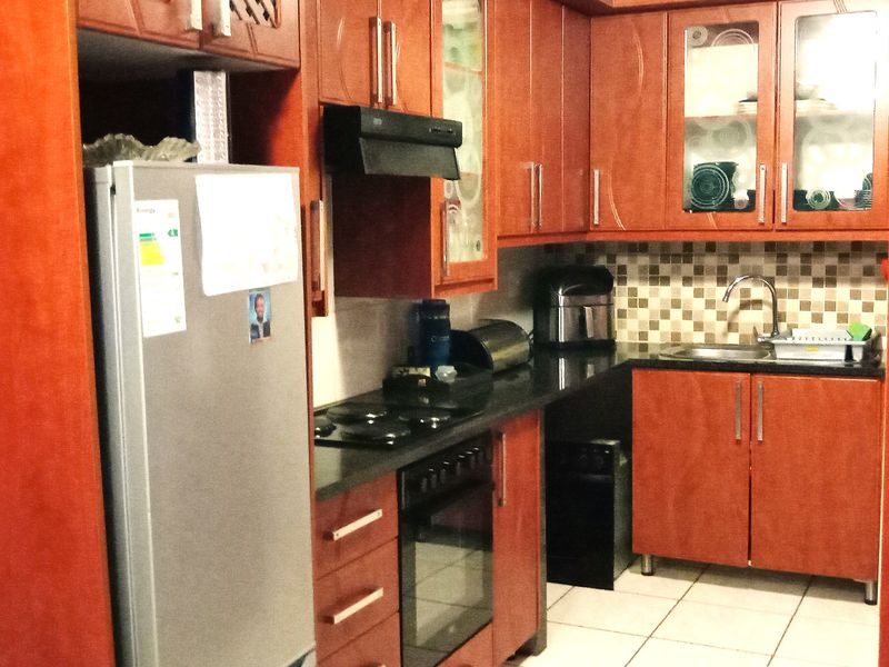 A compact kitchen featuring wood-finish cabinetry, dark countertops, a built-in oven with hob, and a tiled backsplash.