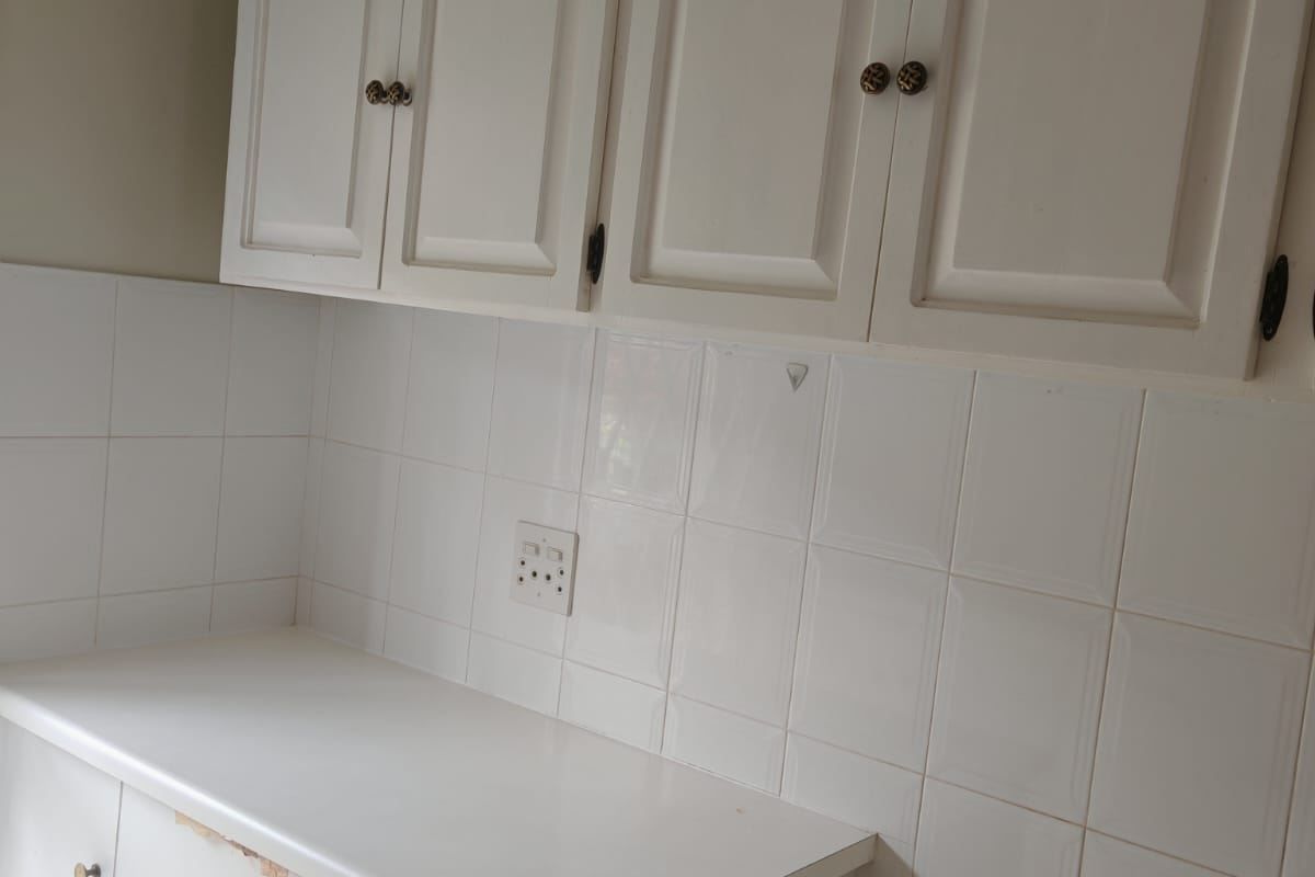 A dated kitchen area featuring white cabinetry, tiled backsplash, and a laminate countertop, currently vacant and ready for renovation.