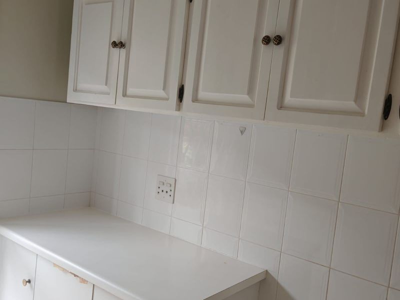A dated kitchen area featuring white cabinetry, tiled backsplash, and a laminate countertop, currently vacant and ready for renovation.