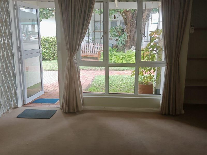 Spacious living area featuring neutral carpeting, built-in shelving, and large windows providing direct access to the garden patio.