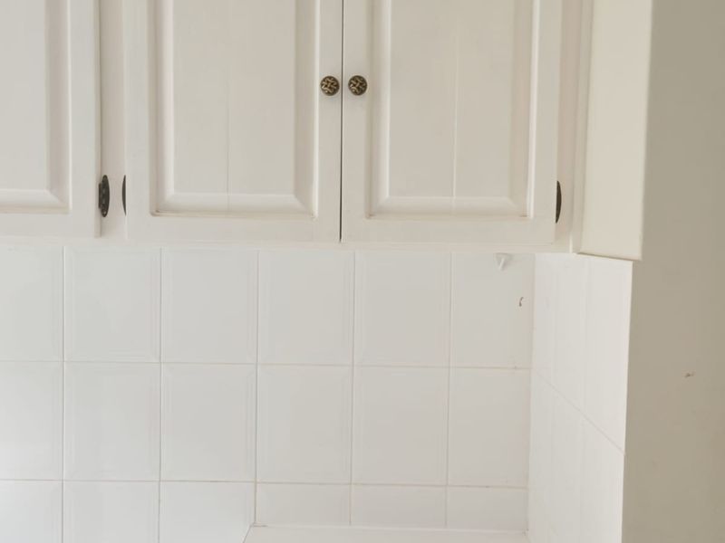 A close-up view of a kitchen area featuring white cabinetry, a tiled backsplash, and a laminate countertop, showing signs of wear.