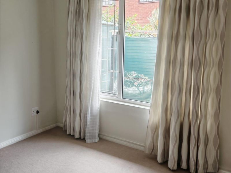 A clean, empty bedroom featuring neutral carpeting, a window with security bars, and installed curtain tracks, ready for personalization.