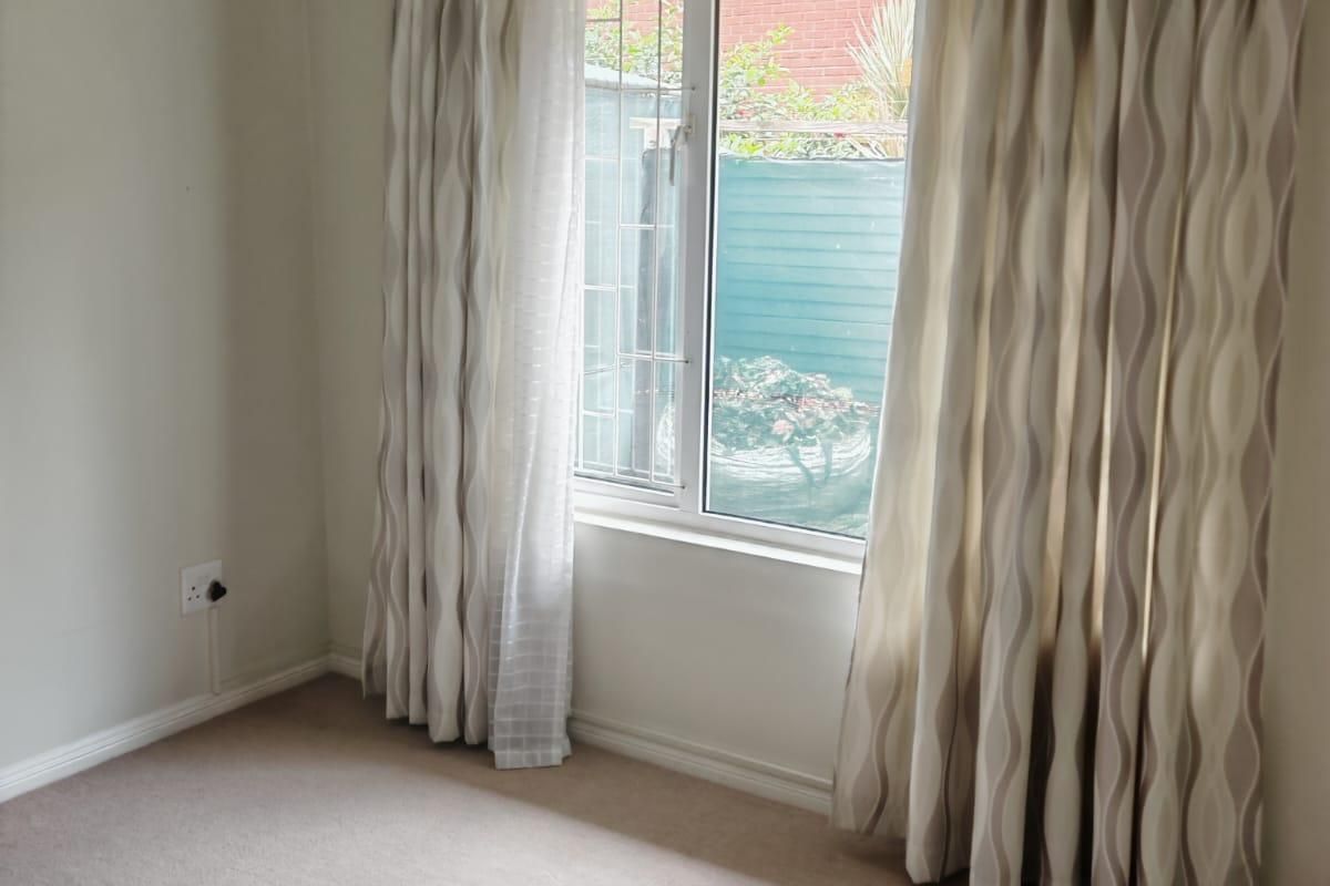 A clean, empty bedroom featuring neutral carpeting, a window with security bars, and installed curtain tracks, ready for personalization.