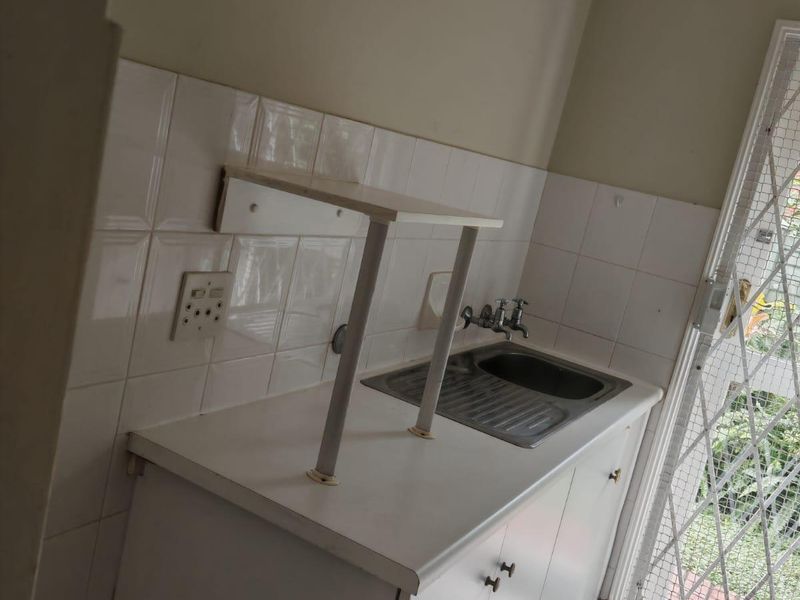 A functional scullery area featuring a stainless steel sink, built-in cabinetry, and tiled splashback, providing a practical utility space with direct exterior access.