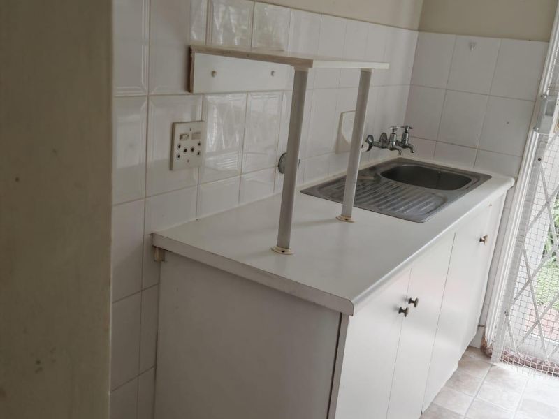 A functional laundry area featuring a stainless steel sink, built-in cabinetry, and tiled splashback, providing a practical utility space.