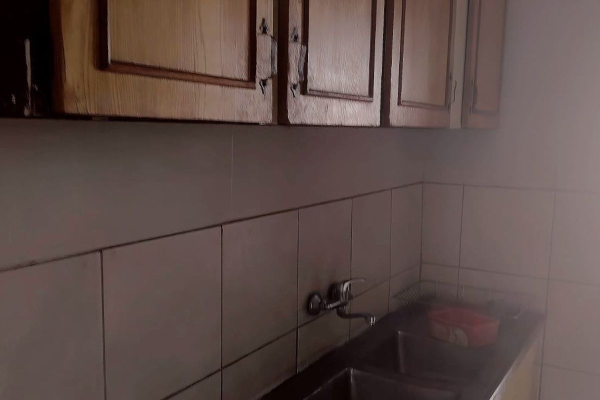 A functional kitchen area featuring wooden wall-mounted cabinetry, a tiled backsplash, and a double stainless steel sink with a faucet.