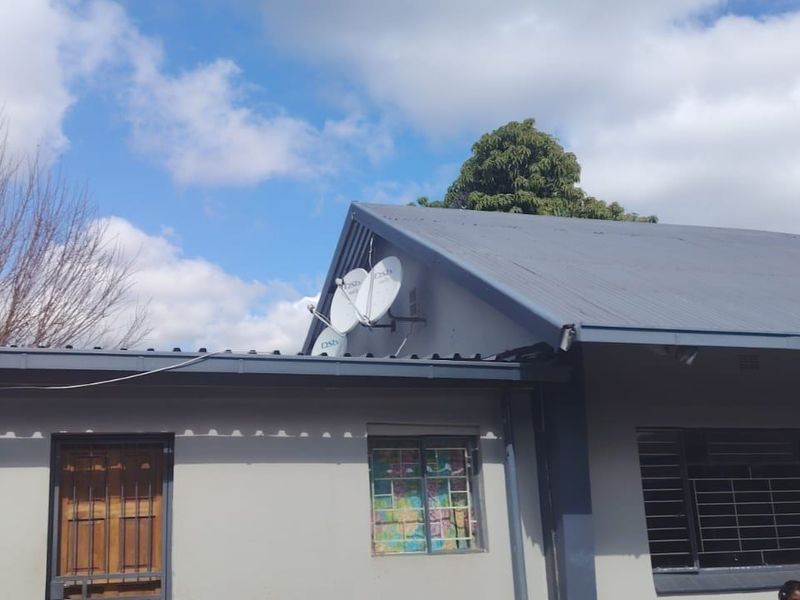 Rear exterior view of the house featuring a corrugated metal roof, security bars on windows, and mounted satellite dishes.