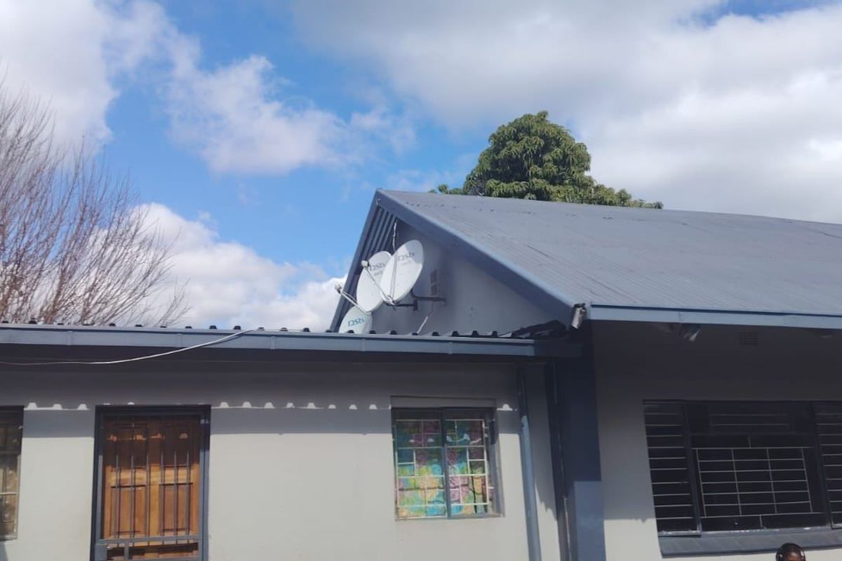 Rear exterior view of the house featuring a corrugated metal roof, security bars on windows, and mounted satellite dishes.