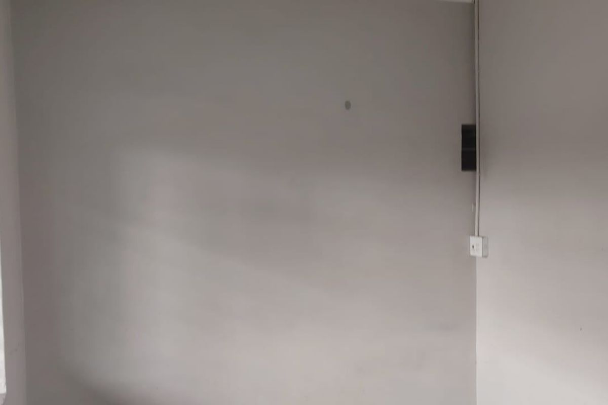 An empty bedroom featuring plain walls, a window with security bars, and visible surface-mounted electrical conduit.