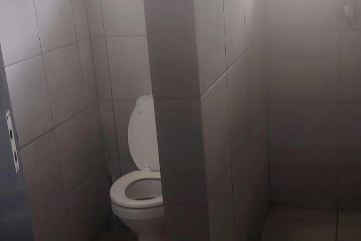 A functional bathroom featuring a toilet and a shower area with tiled walls and flooring, requiring cosmetic updates to improve the overall aesthetic.