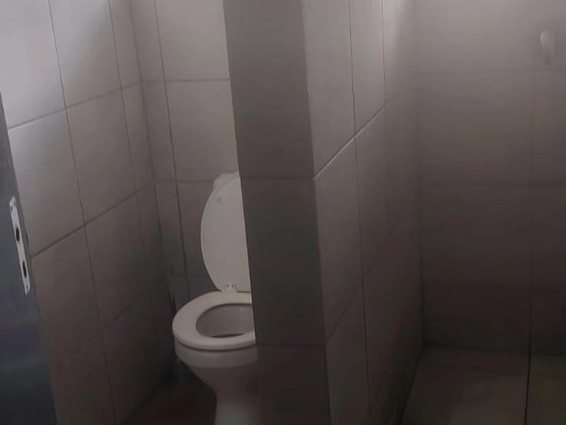 A functional bathroom featuring a toilet and a shower area with tiled walls and flooring, requiring cosmetic updates to improve the overall aesthetic.