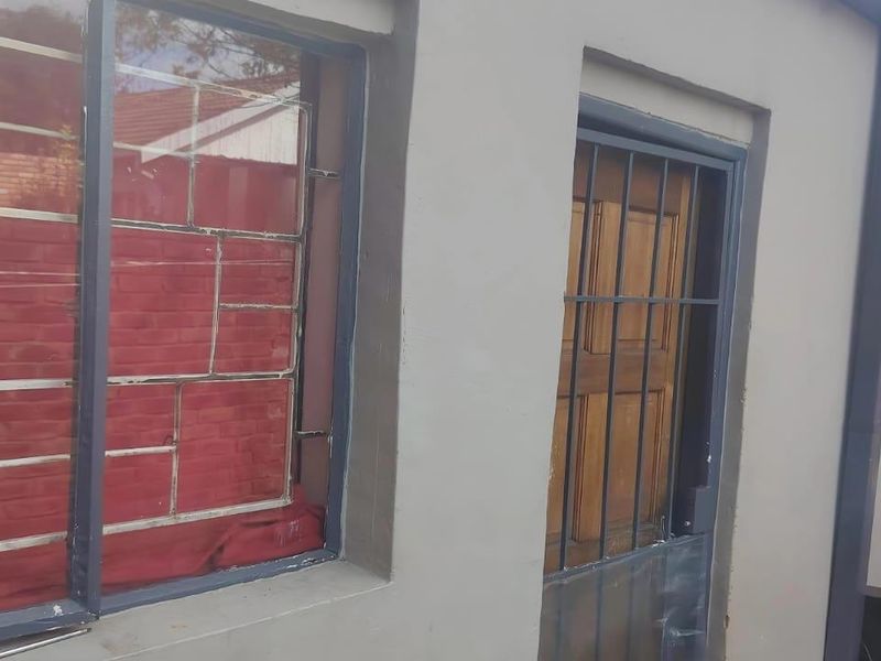 Rear exterior view of the property featuring a timber door, security bars on windows, and an external geyser unit.