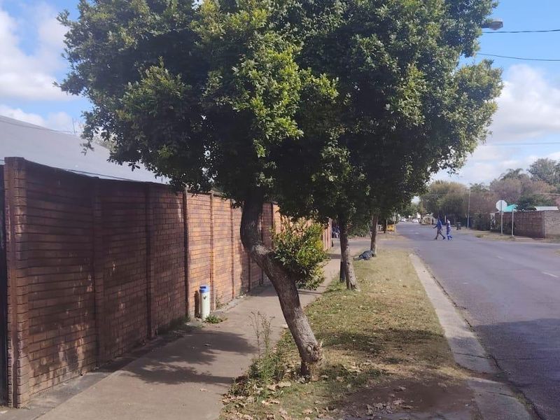 Street view showing the property's exterior brick boundary wall, metal security gate, and adjacent sidewalk in a residential neighborhood.