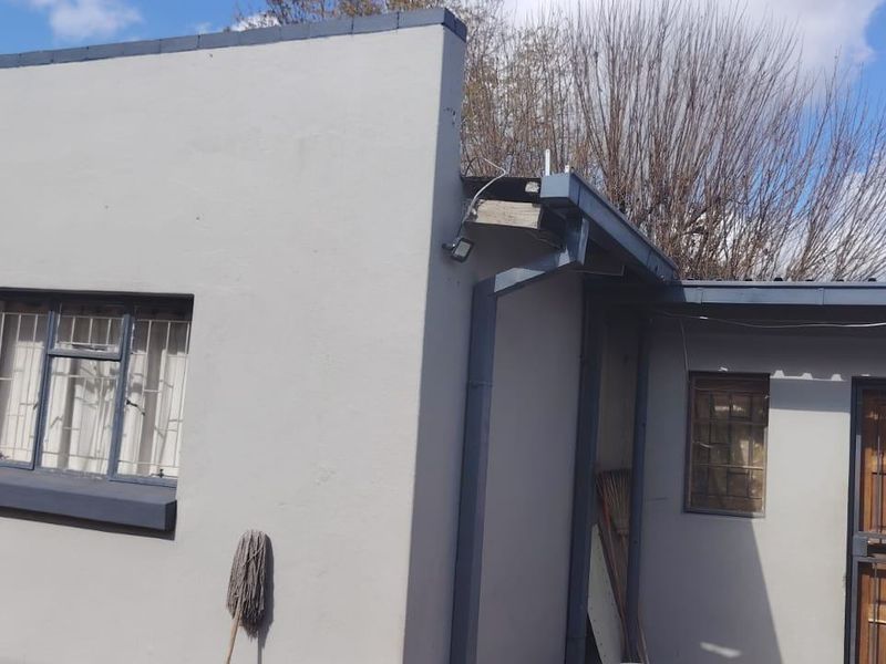 Rear exterior view of the property featuring painted masonry walls, security bars on windows and doors, and functional guttering systems.