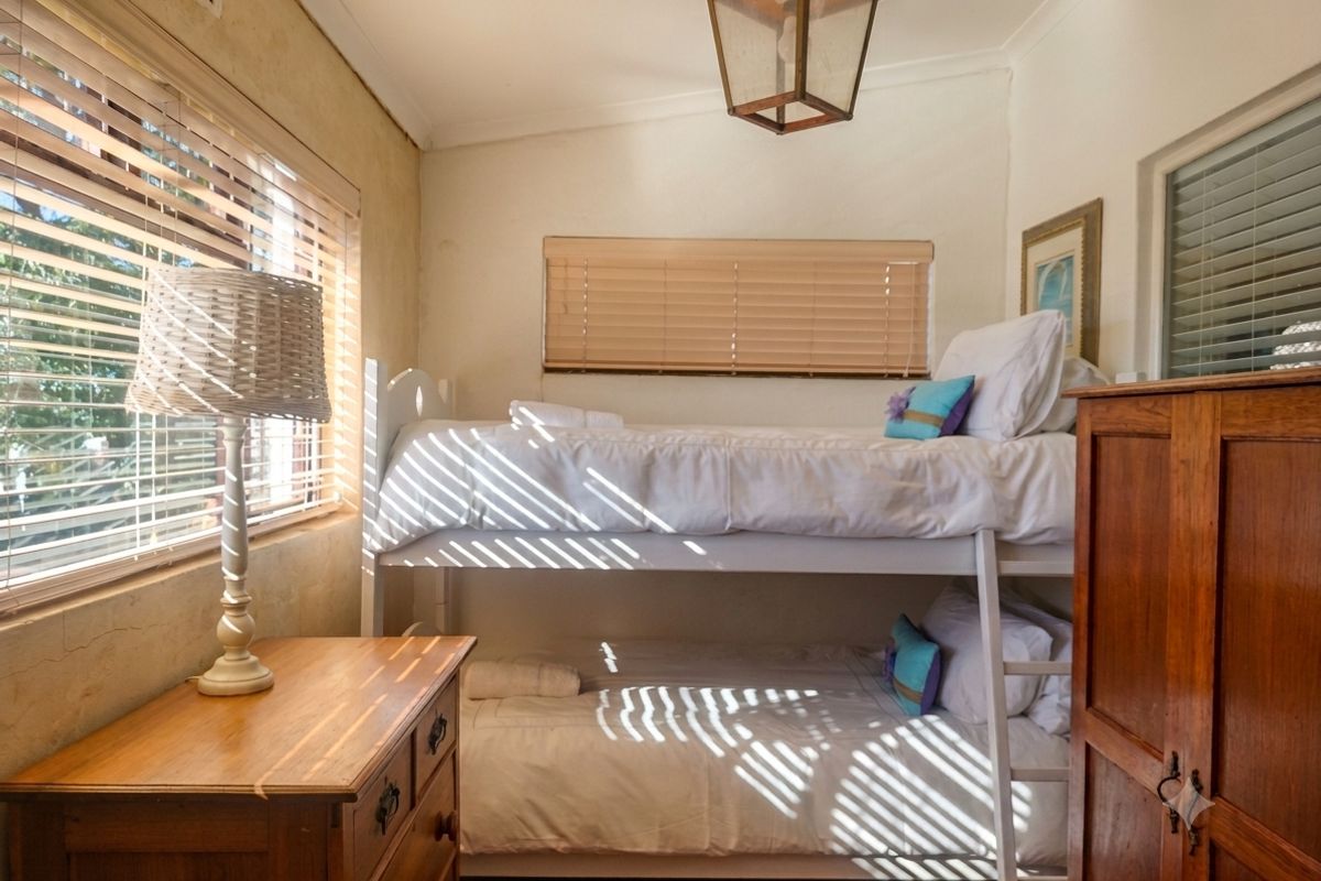 A compact bedroom featuring natural light through venetian blinds, a ceiling light fixture, and visible wall texture.