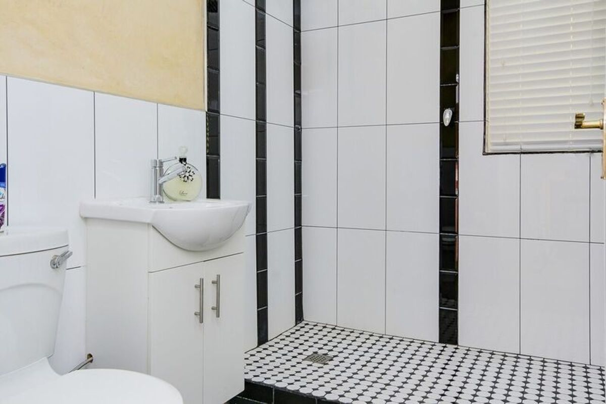 A functional bathroom featuring a vanity basin, toilet, and a tiled shower area with a monochrome tile design.