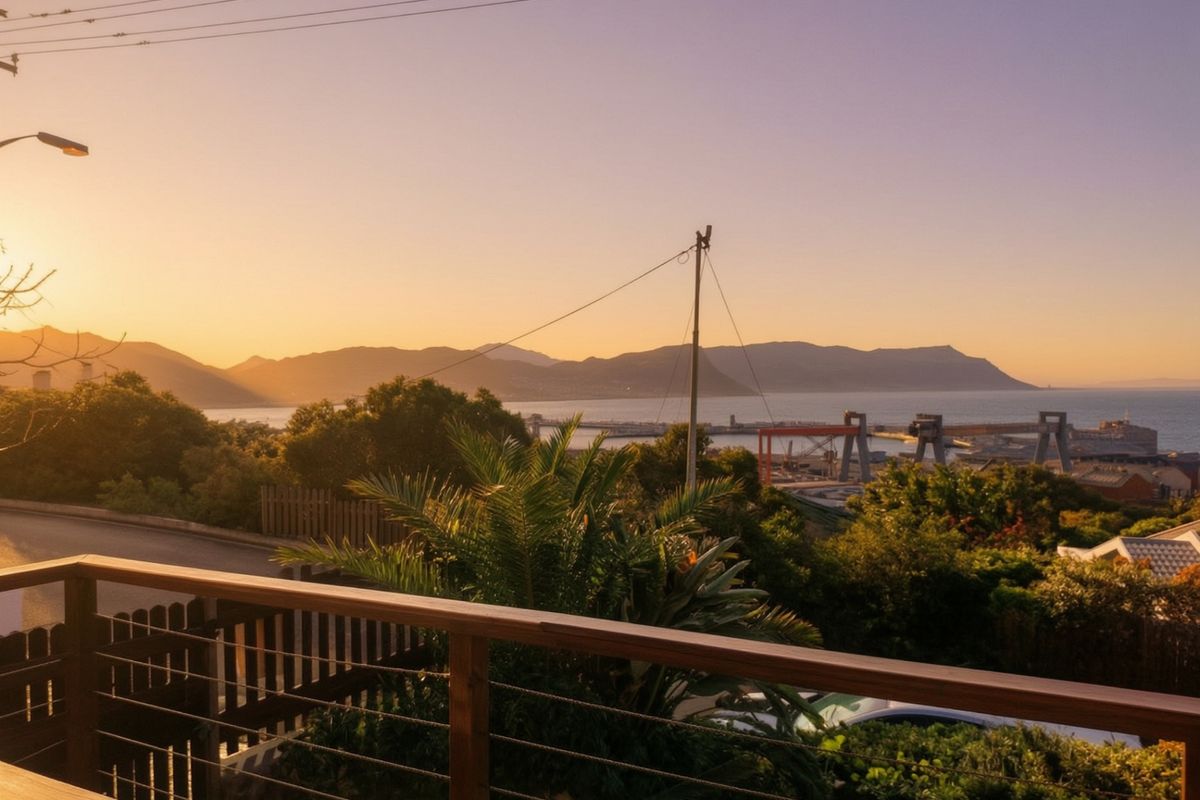 Scenic elevated view overlooking the harbor, coastline, and distant mountains at sunset, framed by a timber and cable balcony railing.