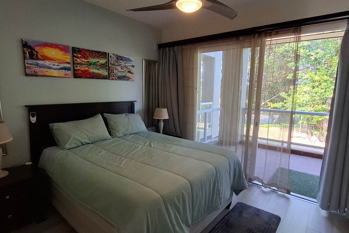 A well-maintained bedroom featuring laminate flooring, a ceiling fan, and large sliding glass doors providing access to an outdoor balcony area.