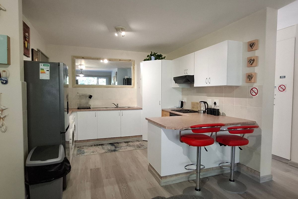 A functional kitchen featuring white cabinetry, laminate countertops, a tiled backsplash, and a breakfast bar area with integrated hob and extractor fan.