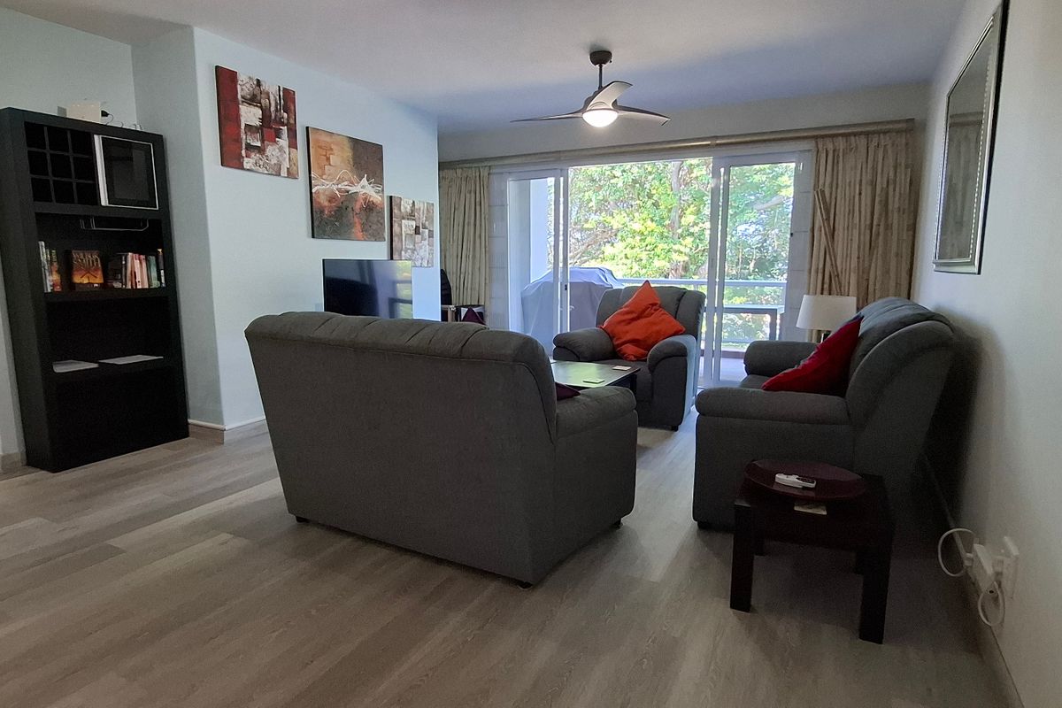A comfortable living room featuring light-toned laminate flooring, a ceiling fan, and large sliding glass doors that provide access to an outdoor balcony area.