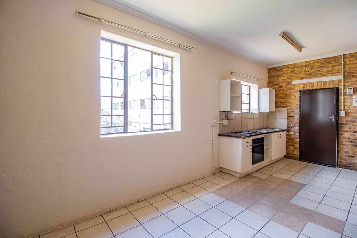 A compact, empty kitchen featuring built-in cabinetry, an oven, hob, tiled flooring, and an exposed brick feature wall.