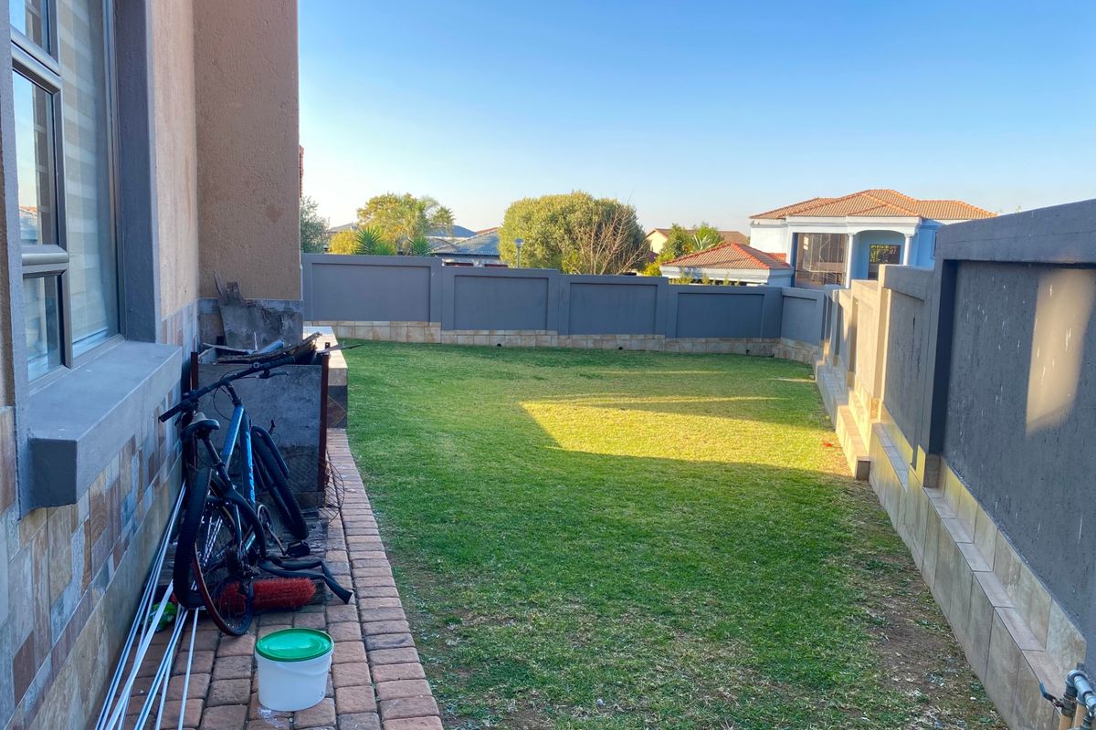 A private rear garden featuring a well-maintained lawn, paved walkway, and secure perimeter walling.