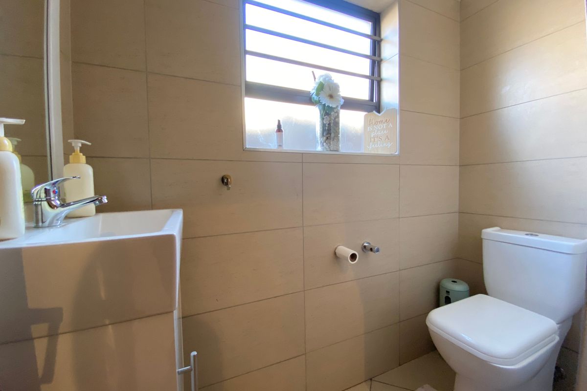 A compact, well-maintained bathroom featuring neutral ceramic wall and floor tiles, a modern vanity basin with chrome mixer, and a standard toilet.