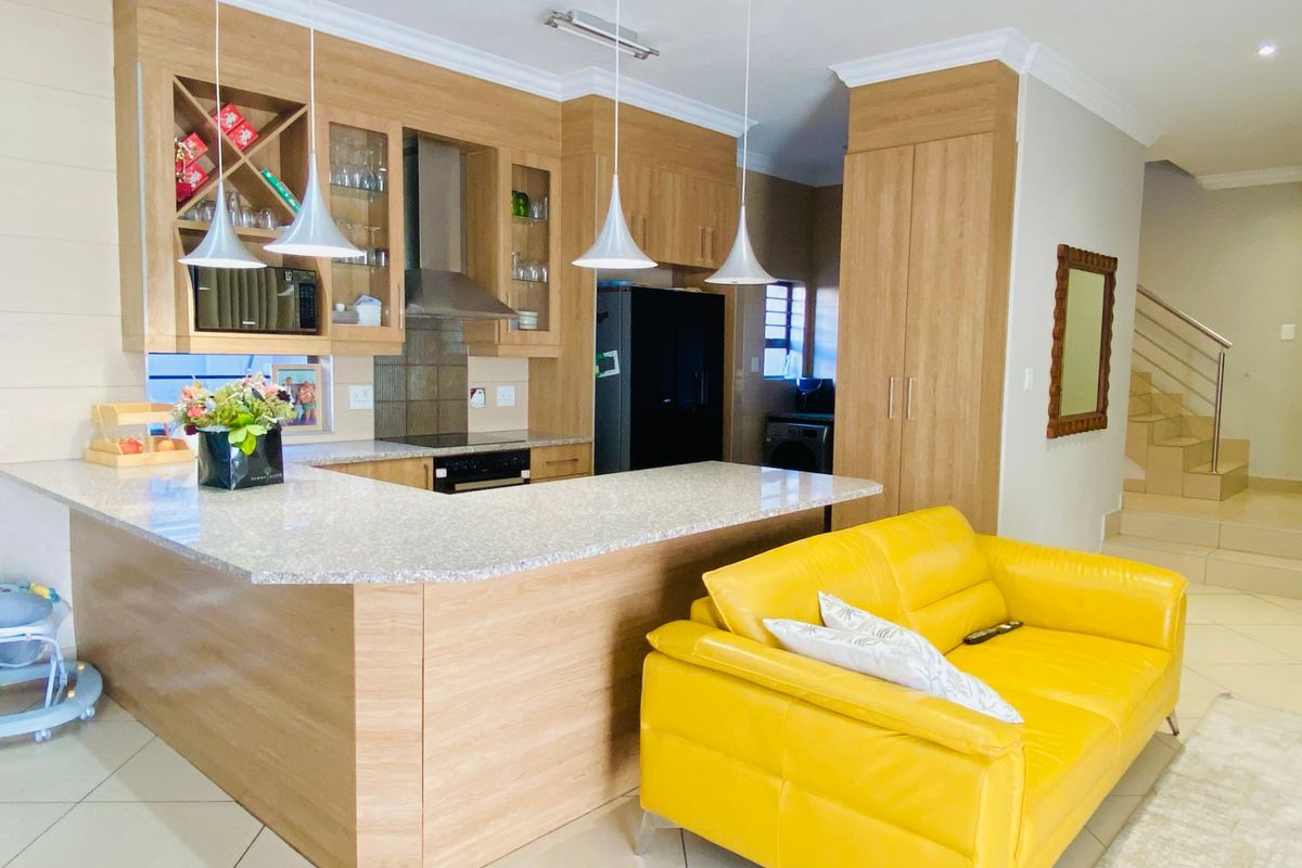 Open-plan kitchen featuring light wood cabinetry, granite countertops, and integrated appliances, seamlessly flowing into the living area with staircase access.