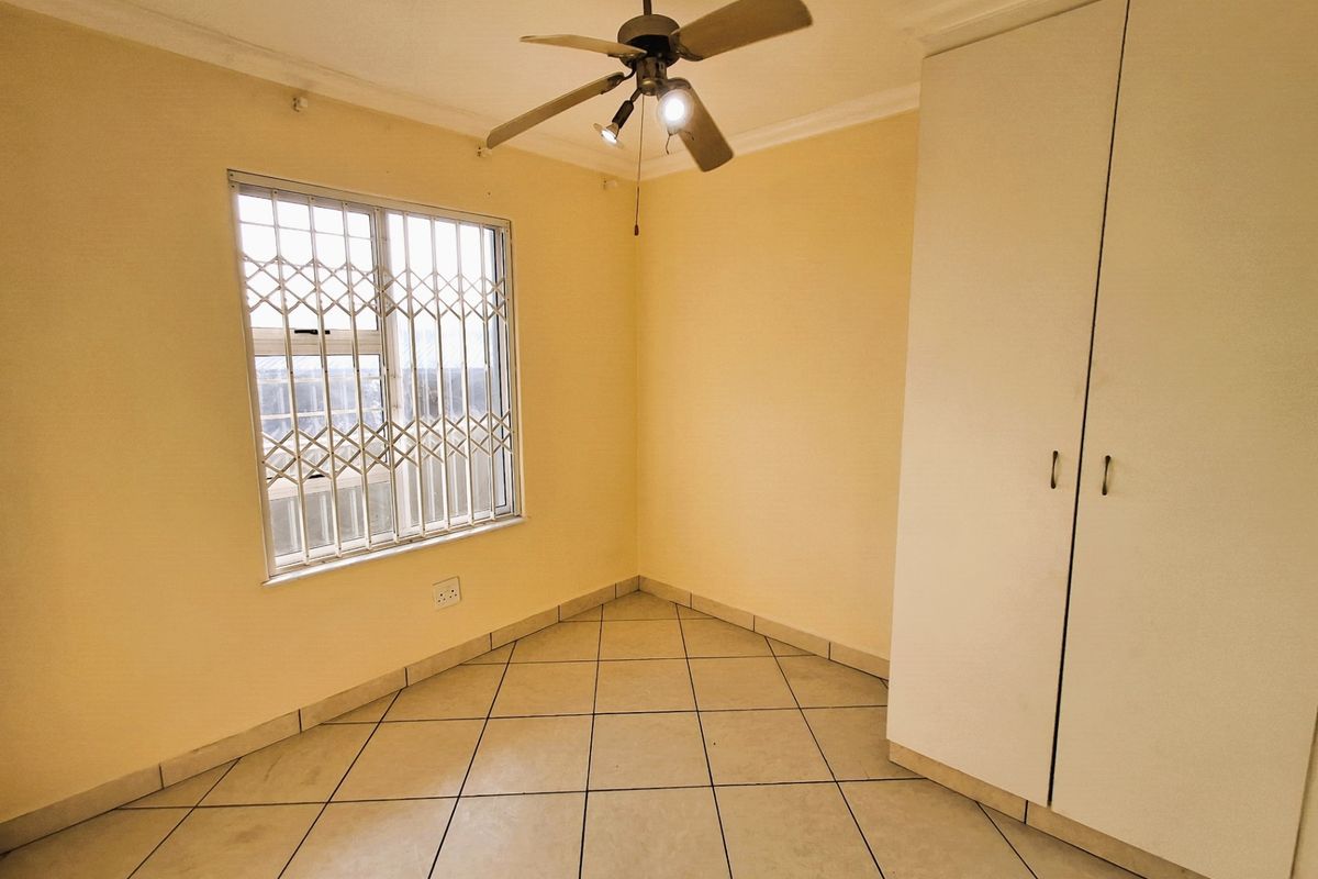 A bright, empty bedroom featuring tiled flooring, a built-in wardrobe, and a ceiling fan with integrated lighting.