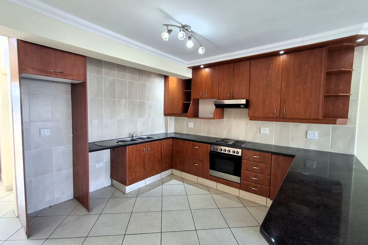 A functional kitchen featuring wooden cabinetry, granite countertops, built-in oven, electric hob, and tiled finishes throughout.