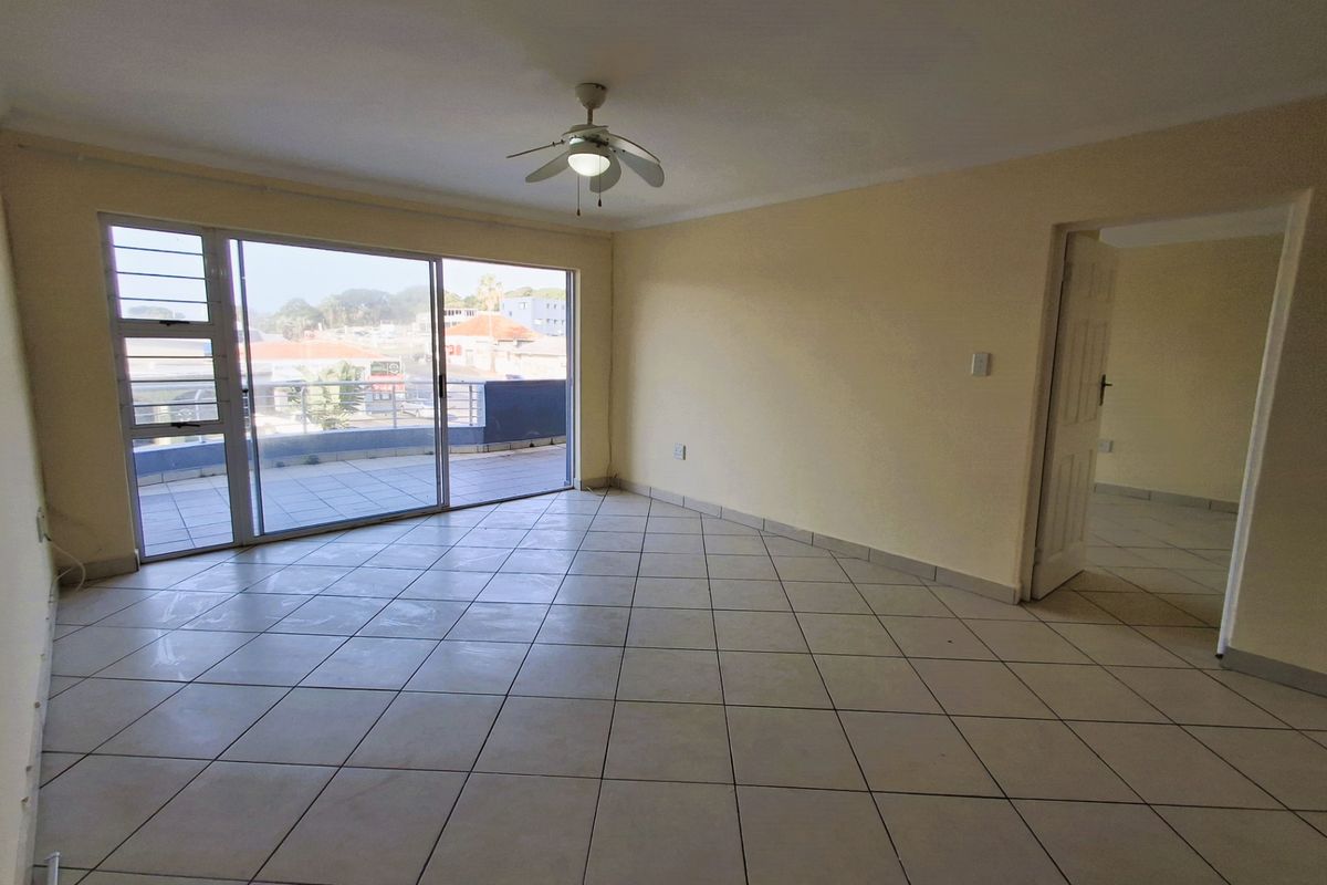 Spacious, empty living area featuring tiled flooring, a ceiling fan, and large sliding glass doors providing access to an outdoor balcony.