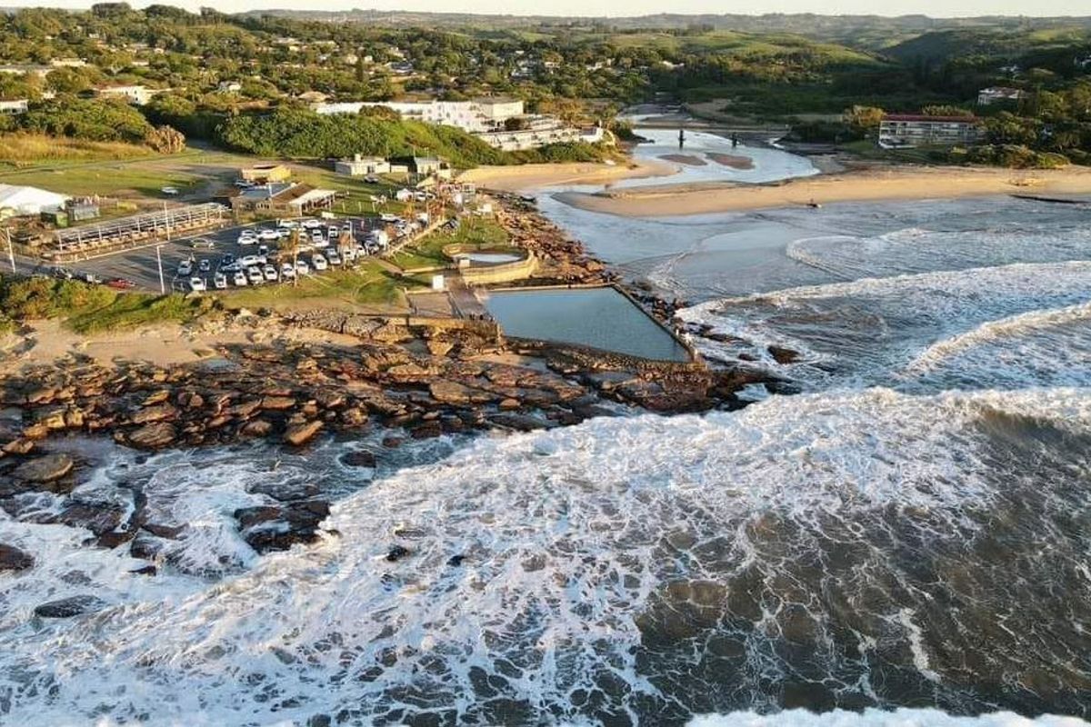An aerial view of the coastal area featuring a natural tidal pool, sandy beach, and surrounding landscape.