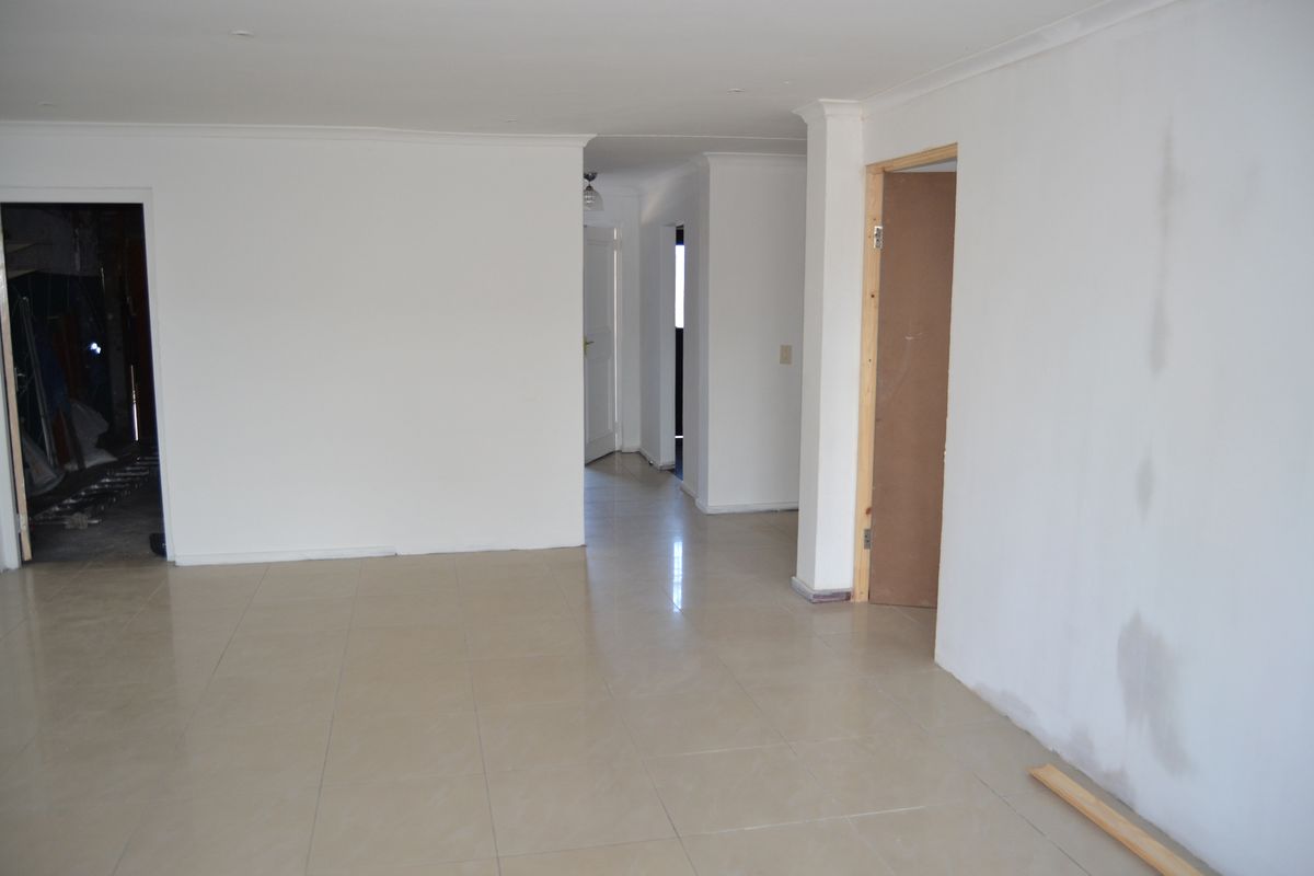 An empty, open-plan living area featuring tiled flooring and recessed lighting, currently undergoing finishing works with visible wall patches and unpainted door frames.