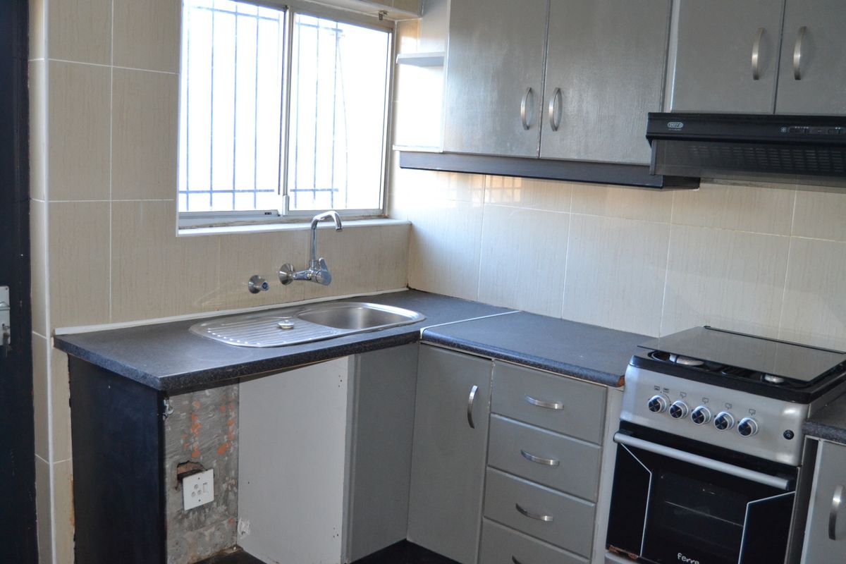 A functional kitchen featuring built-in cabinetry, a stainless steel sink, and tiled splashbacks, currently requiring minor repairs to the lower cabinetry.