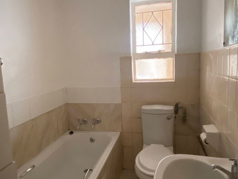 A functional bathroom featuring a bathtub, pedestal basin, and toilet with neutral wall and floor tiling, offering potential for modernization.
