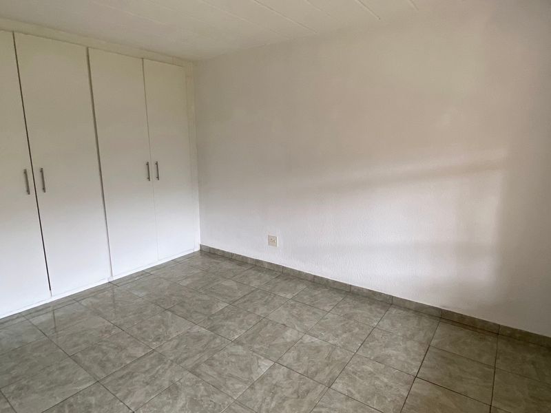 A clean, empty bedroom featuring neutral tiled flooring and ample built-in cupboard storage space.