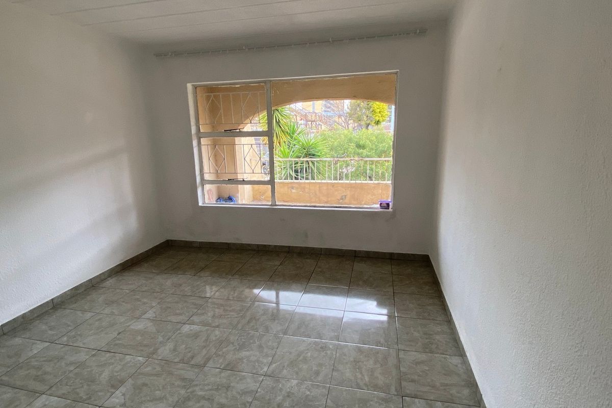 A vacant bedroom featuring tiled flooring and a large window with security bars, offering a view of the exterior balcony area.