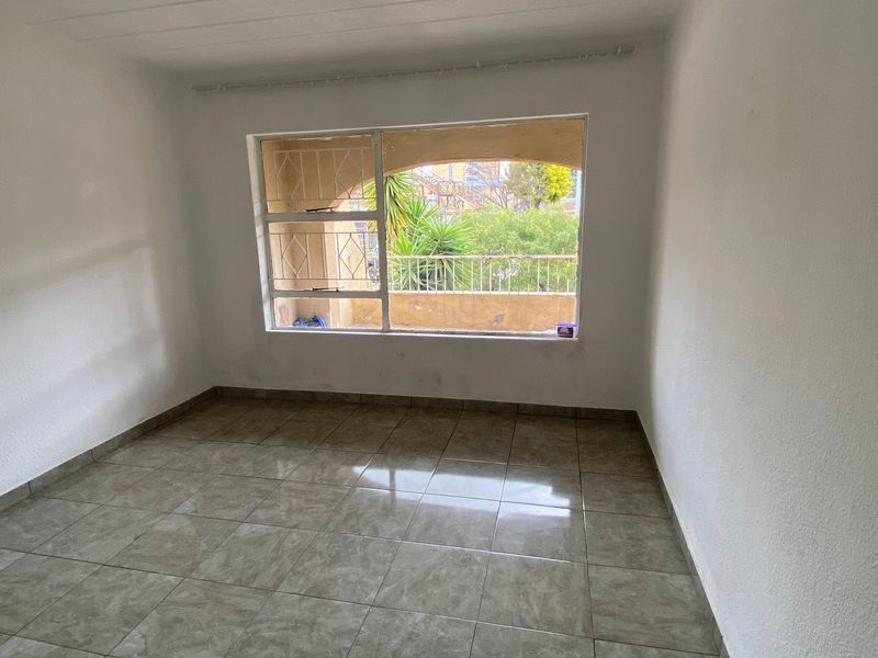 A vacant bedroom featuring tiled flooring and a large window with security bars, offering a view of the exterior balcony area.