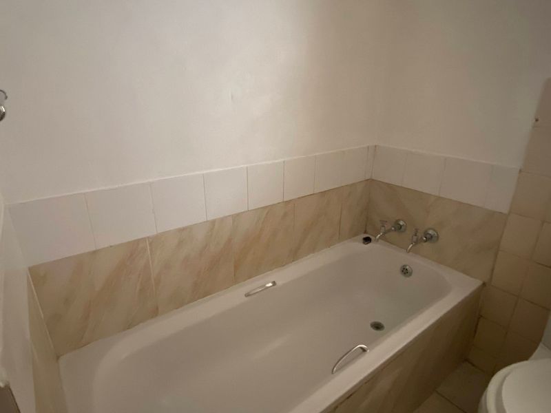 A functional bathroom featuring a standard bathtub, toilet, and tiled splashback, requiring cosmetic updates to improve its overall aesthetic appeal.