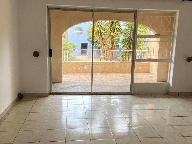 An empty living room featuring tiled flooring and a large sliding glass door that opens onto a covered balcony with an arched design.