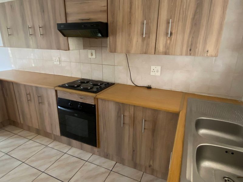 A functional kitchen featuring wood-look laminate cabinetry, built-in oven and hob, double stainless steel sink, and tiled flooring.