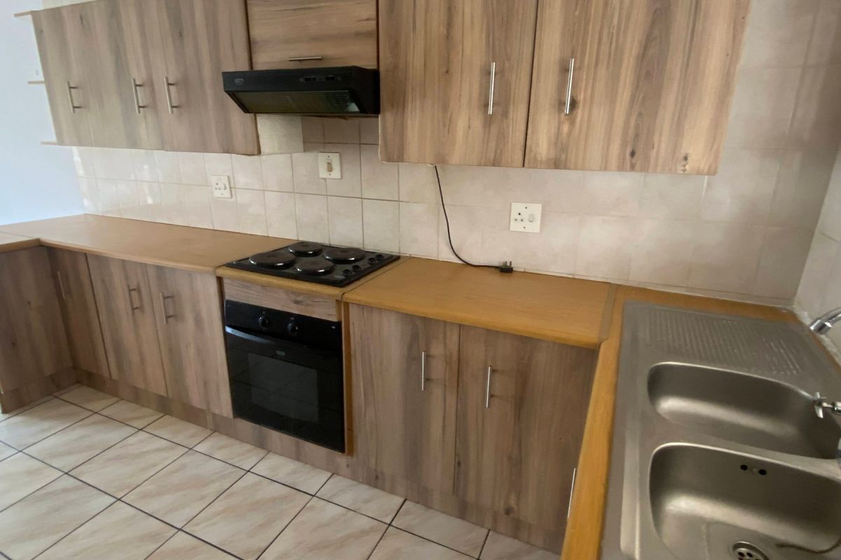A functional kitchen featuring wood-look laminate cabinetry, built-in oven and hob, double stainless steel sink, and tiled flooring.