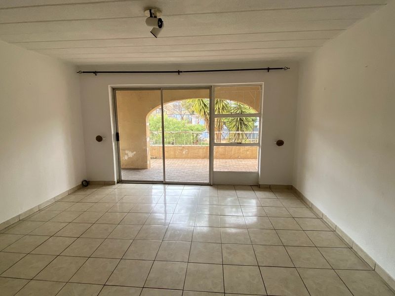 An empty, tiled living room featuring a large sliding glass door that opens onto a private balcony.