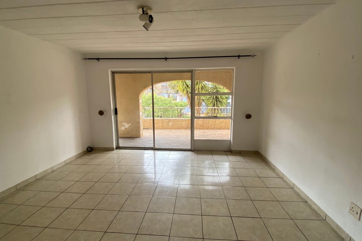 An empty, tiled living room featuring a large sliding glass door that opens onto a private balcony.