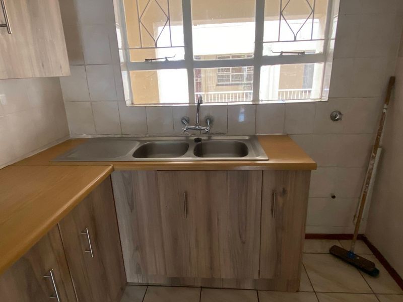 A functional kitchen area featuring wood-look cabinetry, laminate countertops, a double bowl stainless steel sink, and tiled finishes.