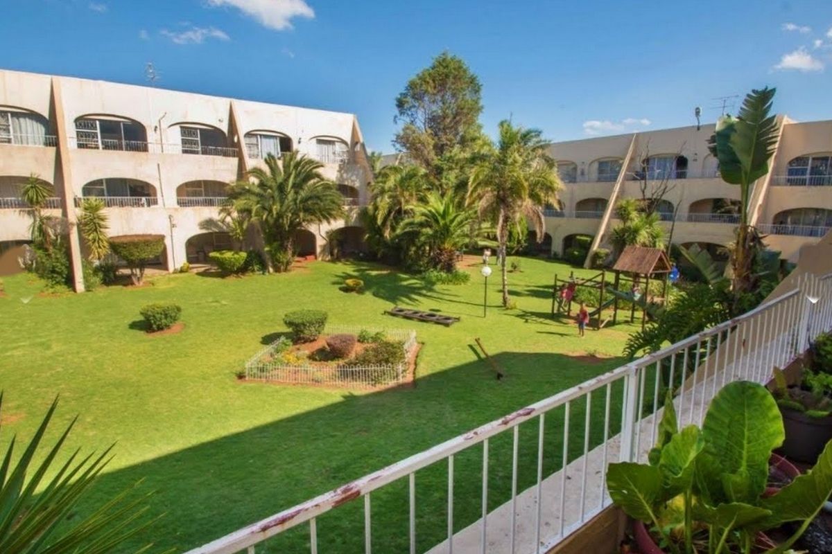 View of a communal garden area surrounded by apartment building facades with arched balconies and established landscaping.
