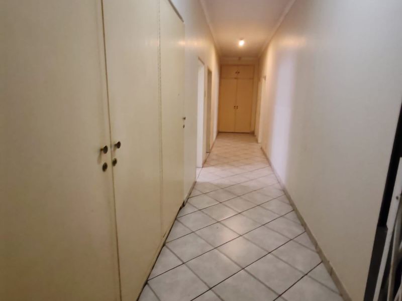 A long, functional hallway featuring neutral tiled flooring and extensive built-in cupboard storage, providing a clean and practical transition space within the home.