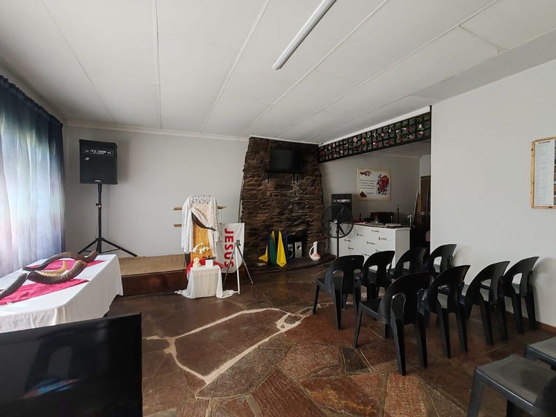 A multi-purpose living space featuring a prominent stone fireplace, rustic flagstone flooring, and a raised wooden platform area.