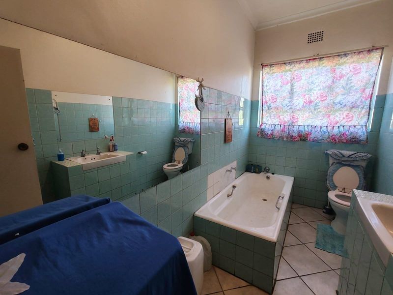 A dated bathroom featuring a built-in bathtub, vanity, and toilet with original light blue wall tiling and ceramic floor tiles.